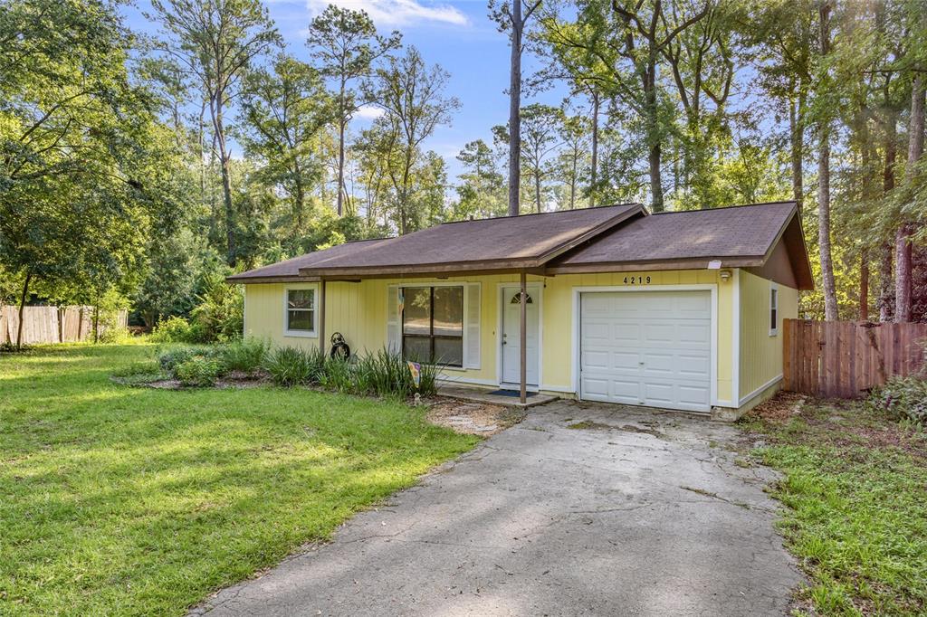 A single-story yellow house with a garage and a concrete driveway sits among trees — 4219 NW 30TH TERRACE, GAINESVILLE, FL