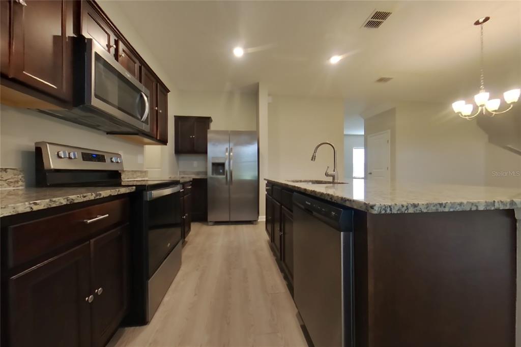 A kitchen features dark wood cabinets, granite countertops, stainless steel appliances, and light wood flooring — 15619 MERLIN AVENUE, MASCOTTE, FL
