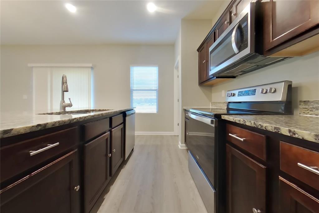 A kitchen features dark wood cabinets, stainless steel appliances, and granite countertops — 15619 MERLIN AVENUE, MASCOTTE, FL