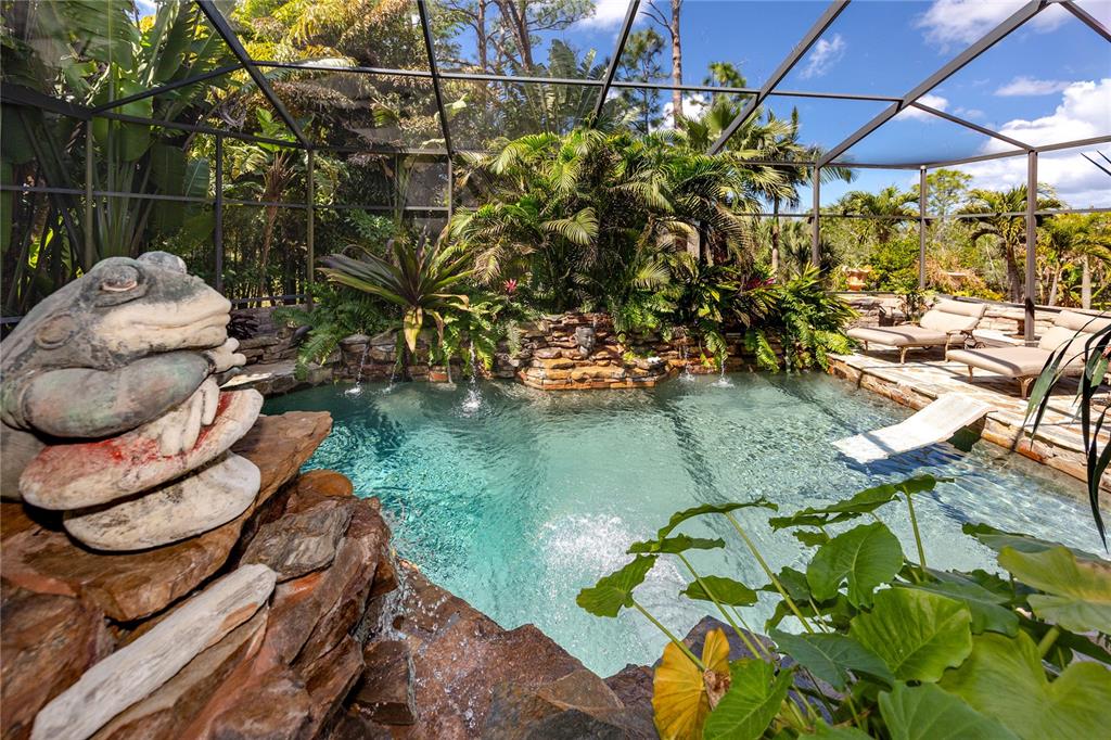 A screened-in swimming pool features a rock waterfall, lush tropical landscaping, and lounge chairs — 2780 LONG PUTT COURT, PALM HARBOR, FL