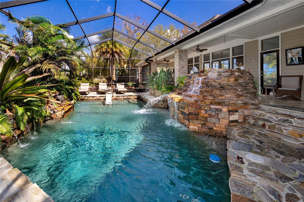 A screened-in pool area features a stone waterfall, tropical landscaping, and a stone patio — 2780 LONG PUTT COURT, PALM HARBOR, FL
