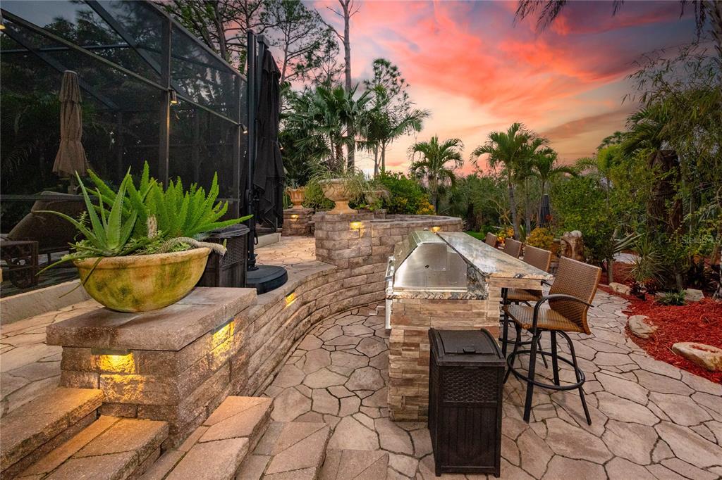 An outdoor patio features a stone bar with a grill, seating, and landscape lighting at sunset — 2780 LONG PUTT COURT, PALM HARBOR, FL