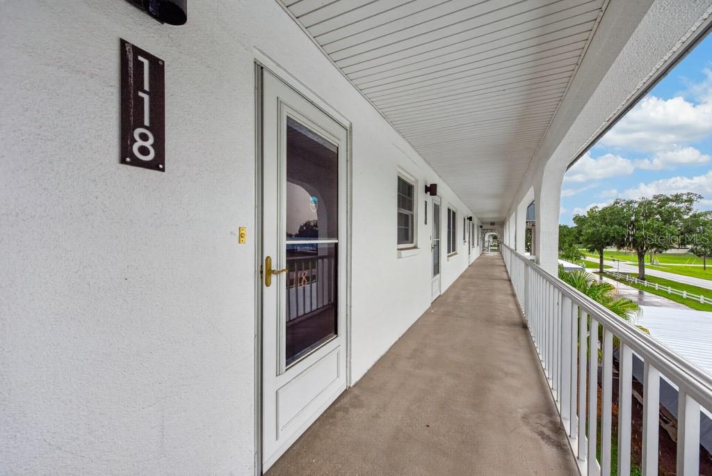 An exterior walkway with white railings leads past several unit doors on a sunny day — 4801 AIRPORT ROAD UNIT 118, ZEPHYRHILLS, FL