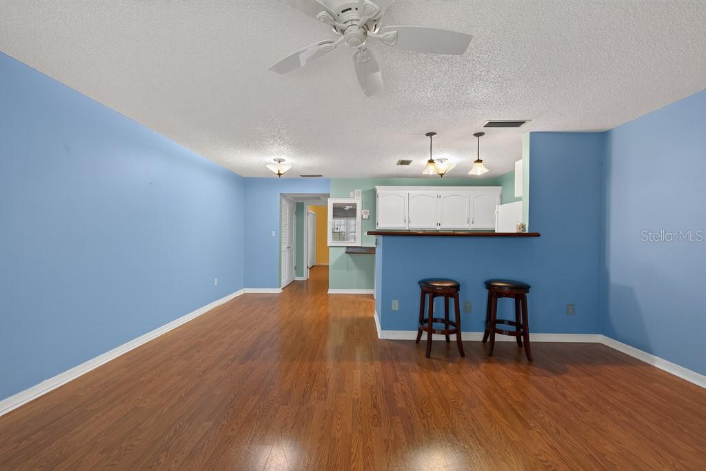 A living room with blue walls, wood-look flooring, and a kitchen breakfast bar with stools — 4801 AIRPORT ROAD UNIT 118, ZEPHYRHILLS, FL