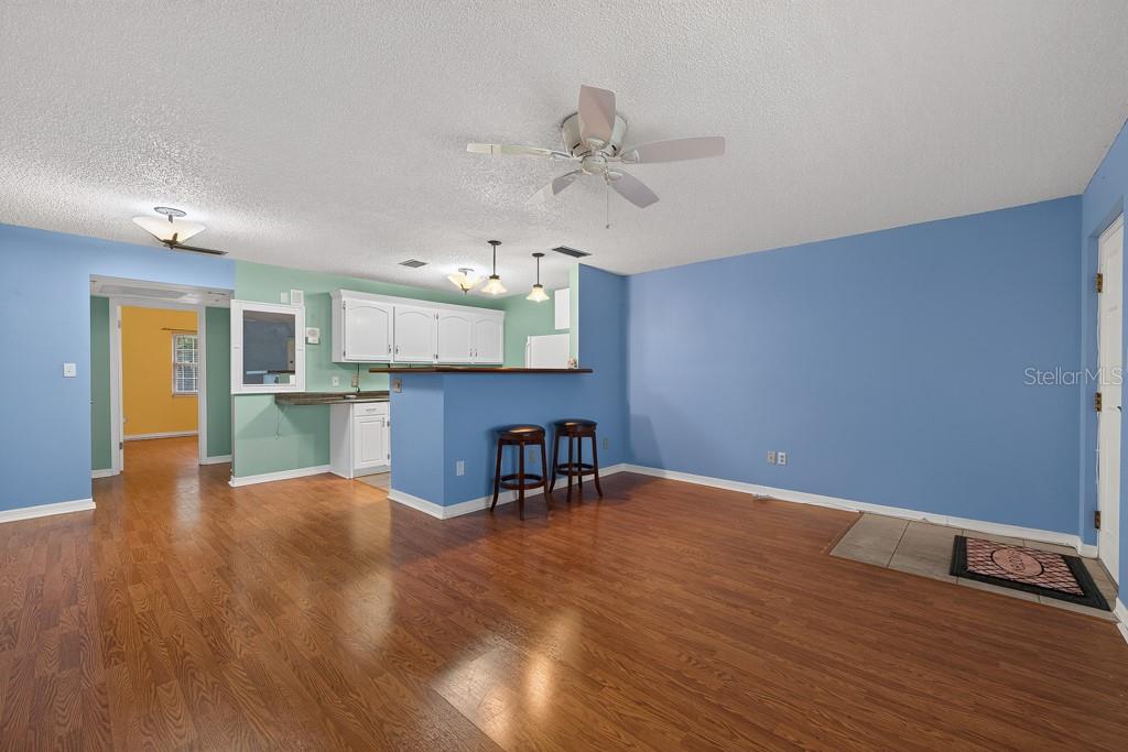 A living room with blue walls, wood flooring, and a kitchen breakfast bar with stools — 4801 AIRPORT ROAD UNIT 118, ZEPHYRHILLS, FL