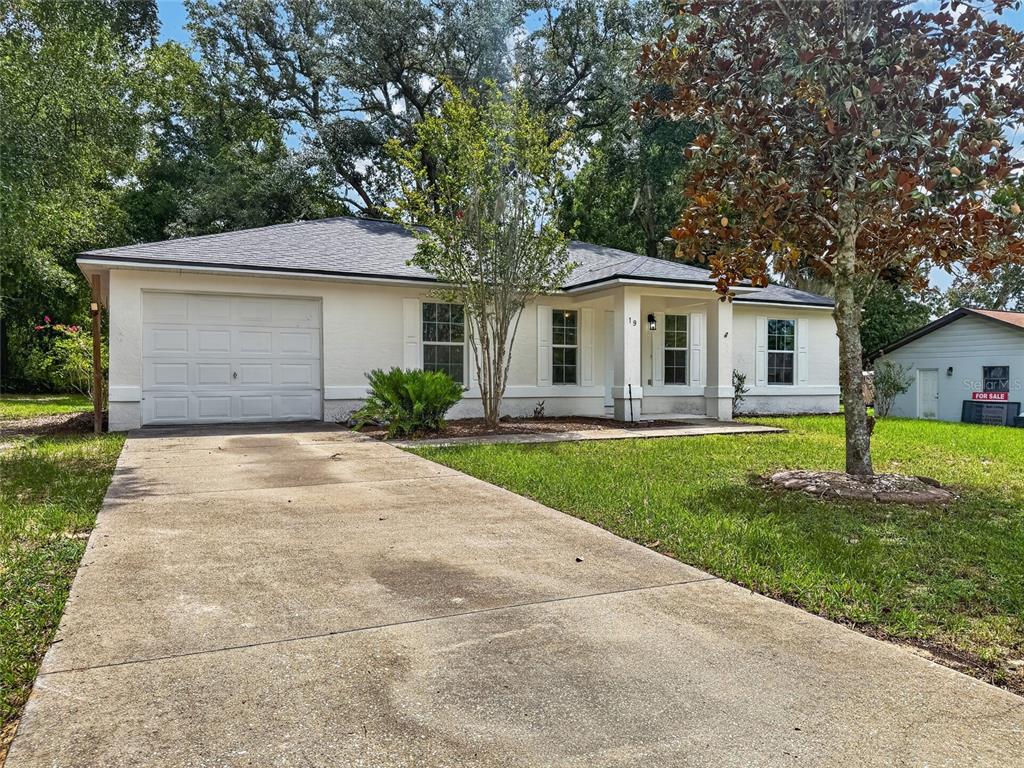 A single-story white house with a concrete driveway, a garage, and a front porch — 19 JUNIPER PASS TRACK, OCALA, FL