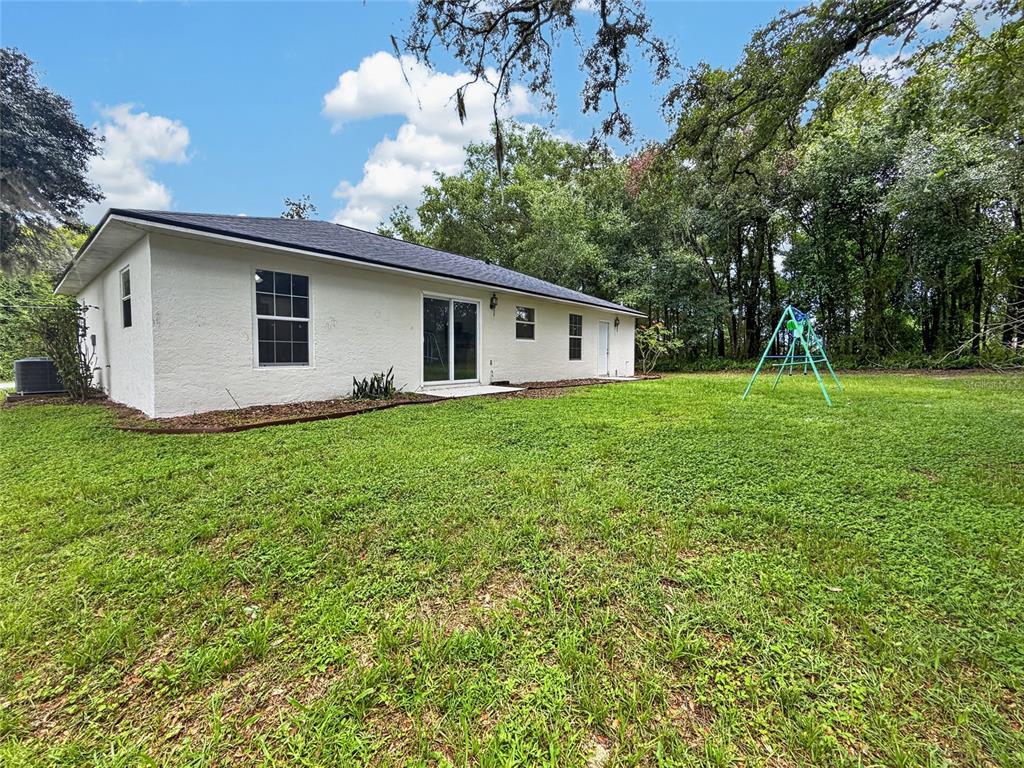 A white, single-story house with a dark roof sits on a grassy lot with trees — 19 JUNIPER PASS TRACK, OCALA, FL