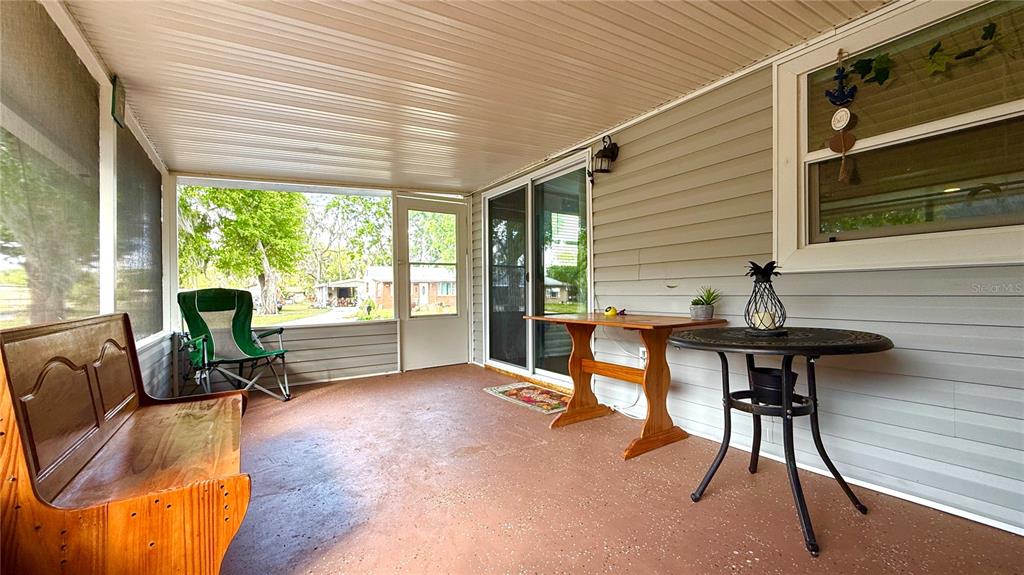 A covered porch features a wooden bench, a small table, and a screen enclosure — 111 NE PALENCIA ROAD, AUBURNDALE, FL