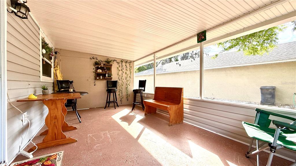 A screened-in porch features a wooden table, bench, bar stools, and a concrete floor — 111 NE PALENCIA ROAD, AUBURNDALE, FL