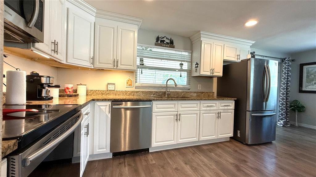 A kitchen features white cabinets, granite countertops, stainless steel appliances, and wood-look flooring — 111 NE PALENCIA ROAD, AUBURNDALE, FL