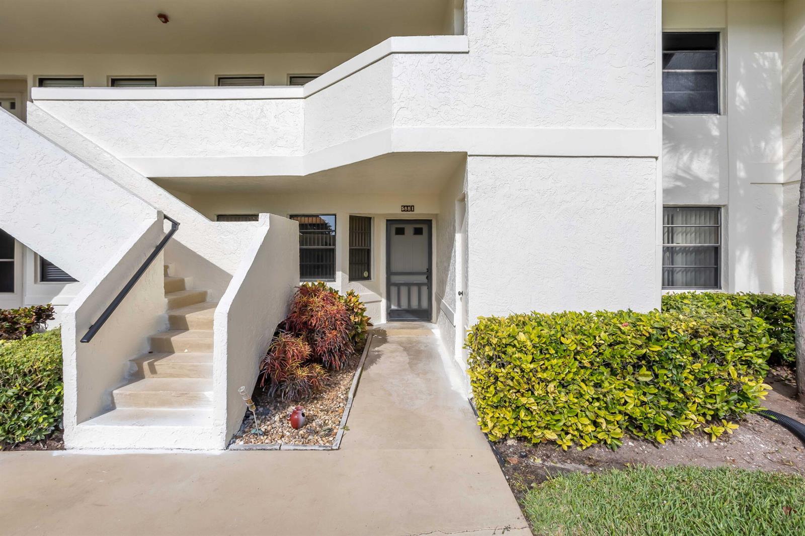 A ground-level apartment entrance features a concrete walkway, stairs, and a small garden bed — 5881 Parkwalk Drive, Boynton Beach FL 33472, BOYNTON BEACH, FL