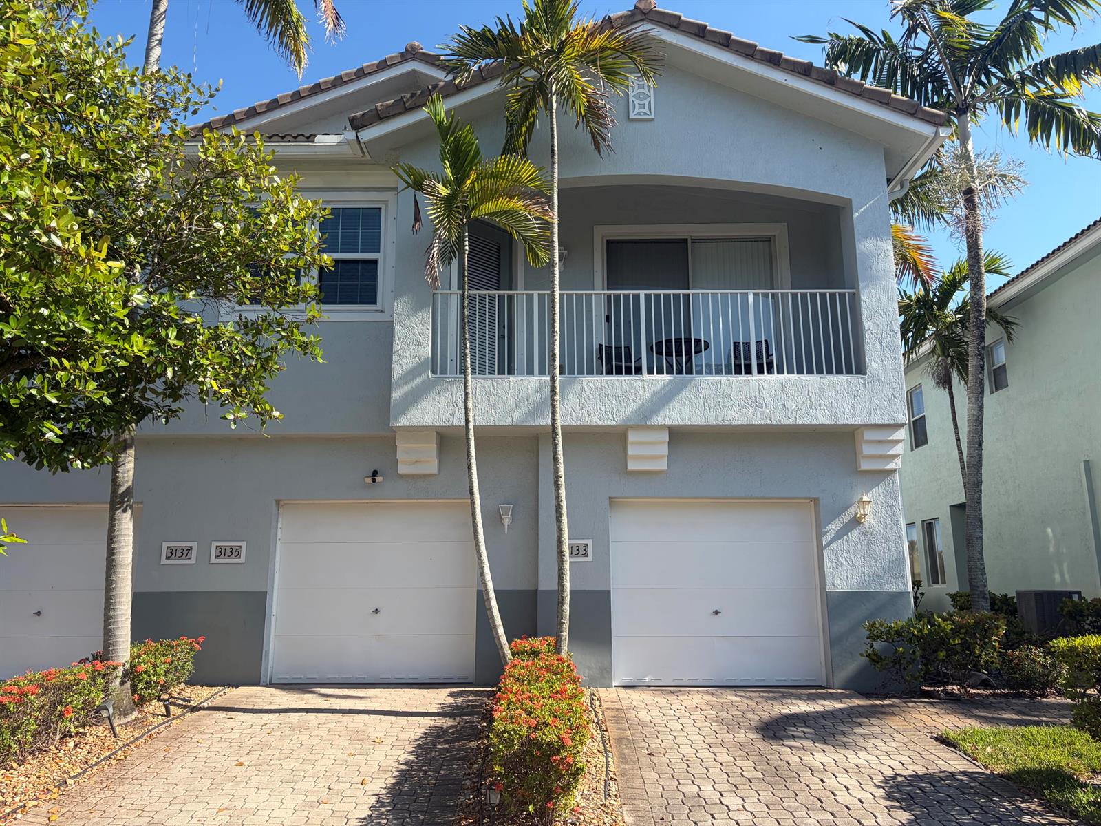A two-story residential building features two white garage doors, a balcony, and palm trees — 3133 Laurel Ridge Circle, West Palm Beach FL 33404, WEST PALM BEACH, FL