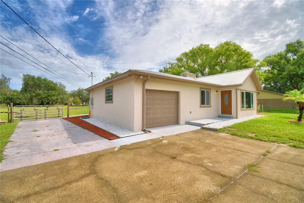 A single-story house with a tan stucco exterior, a metal roof, and a concrete driveway — 8704 TOM COSTINE ROAD, LAKELAND, FL
