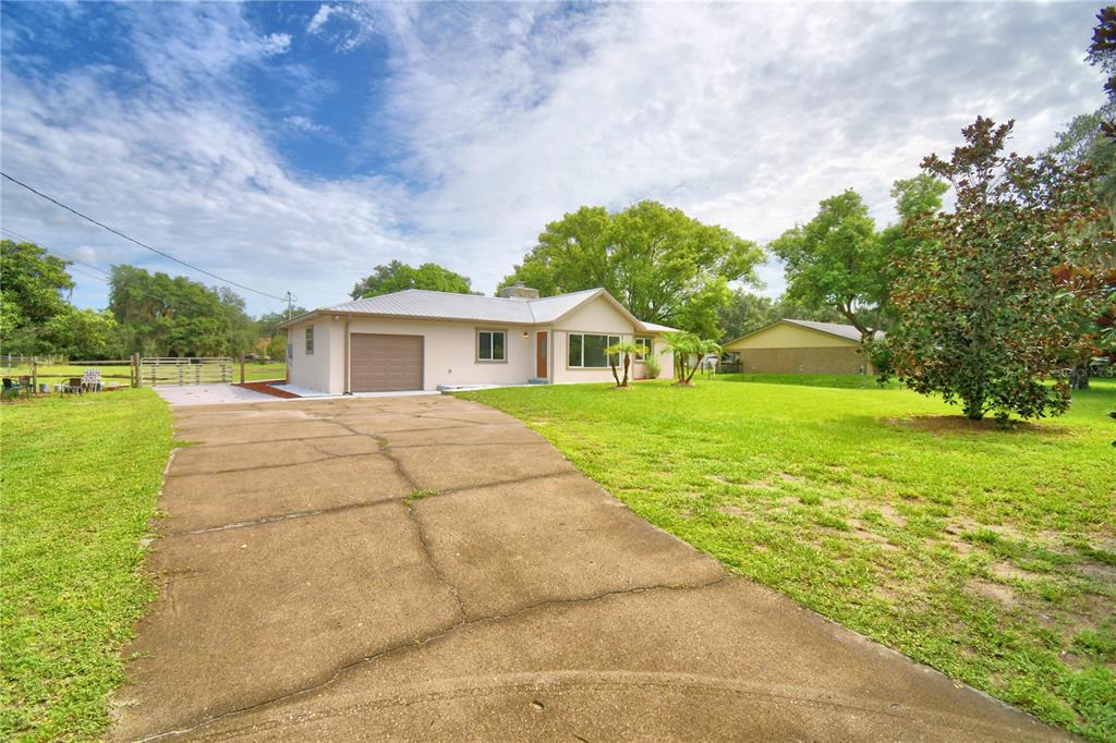 A single-story house with a metal roof, concrete driveway, and a large grassy front yard — 8704 TOM COSTINE ROAD, LAKELAND, FL