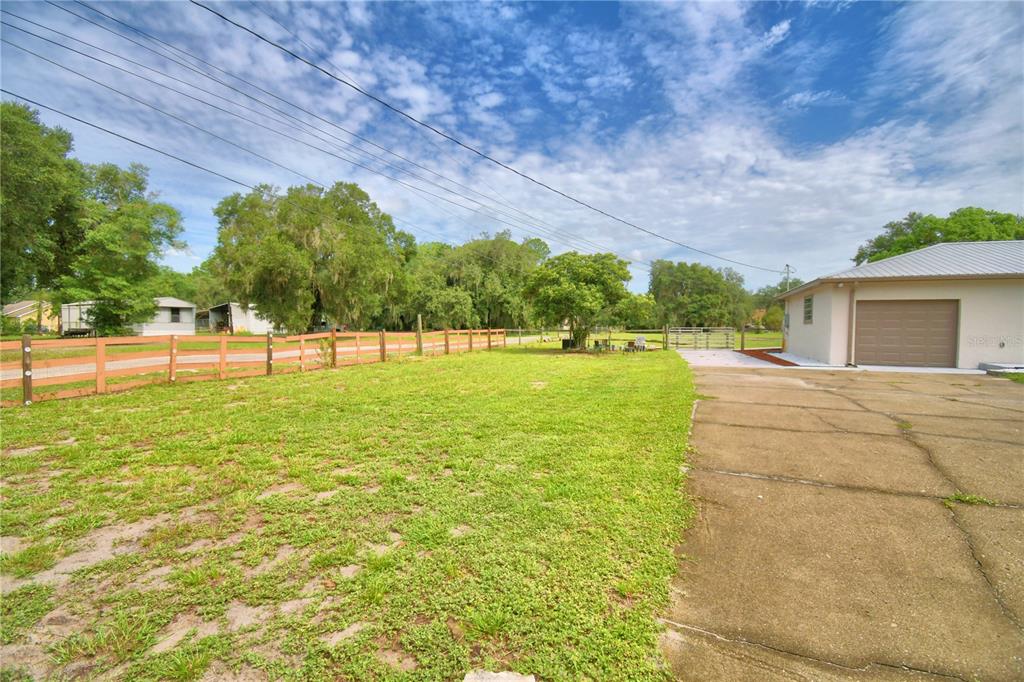 A grassy yard with a wooden fence and a concrete driveway leading to a garage — 8704 TOM COSTINE ROAD, LAKELAND, FL