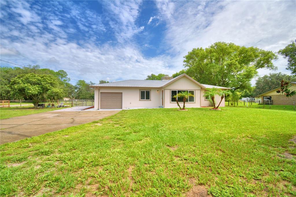 A single-story house with a metal roof, attached garage, and a large front lawn — 8704 TOM COSTINE ROAD, LAKELAND, FL
