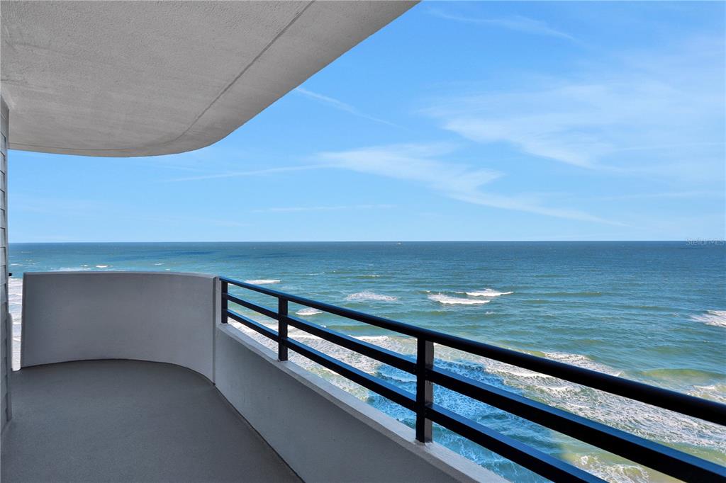 A curved balcony with a black metal railing overlooks the ocean under a blue sky — 1420 N ATLANTIC AVENUE UNIT 901, DAYTONA BEACH, FL