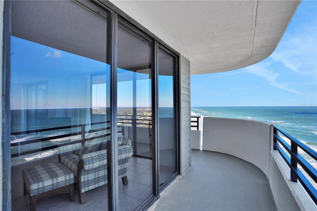A curved balcony with a metal railing overlooks the ocean next to a glass-enclosed room — 1420 N ATLANTIC AVENUE UNIT 901, DAYTONA BEACH, FL
