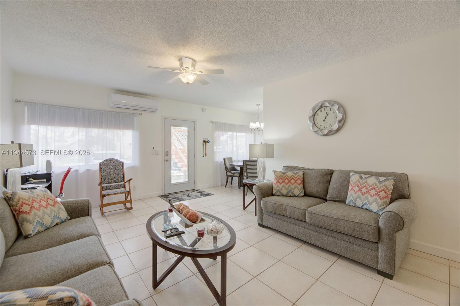 A living room features tiled floors, two gray sofas, a glass coffee table, and a clock — 800 SW 11th Ave # 9A, Hallandale Beach FL 33009, HALLANDALE BEACH, FL