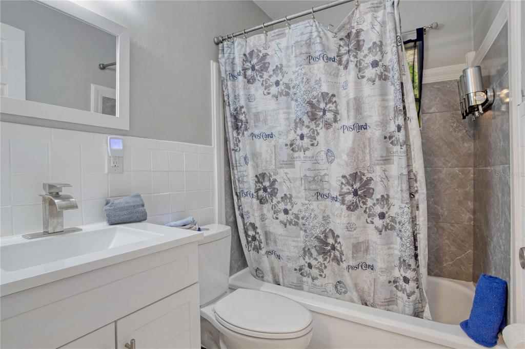 A bathroom features a white vanity, a toilet, and a bathtub with a floral shower curtain — 7329 ROYAL PALM DRIVE, NEW PORT RICHEY, FL
