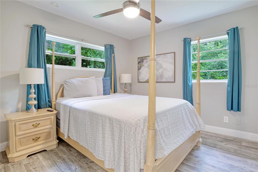 A bedroom features a four-poster bed, light wood furniture, teal curtains, and light gray flooring — 7329 ROYAL PALM DRIVE, NEW PORT RICHEY, FL