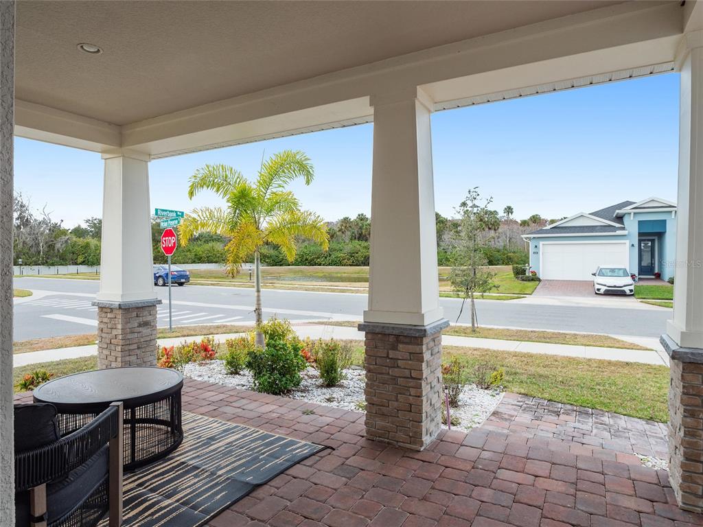 A covered brick porch features stone-based columns and a view of a suburban street — 3437 MCLAIN PRESERVE POINT, SANFORD, FL