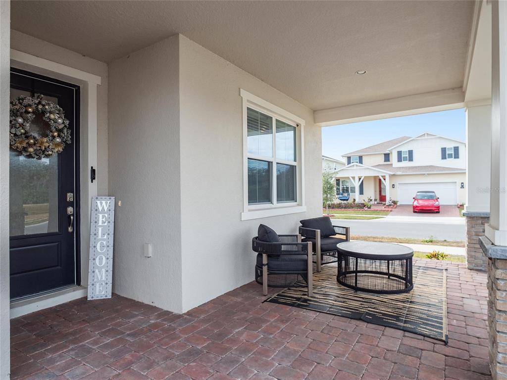 A covered front porch features brick pavers, two dark chairs, a round table, and a door — 3437 MCLAIN PRESERVE POINT, SANFORD, FL