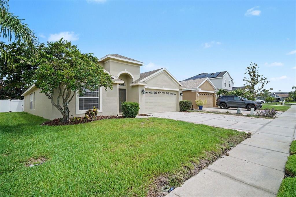A single-story suburban house with a tan stucco exterior, a two-car garage, and a lawn — 2519 BIG PINE DRIVE, HOLIDAY, FL