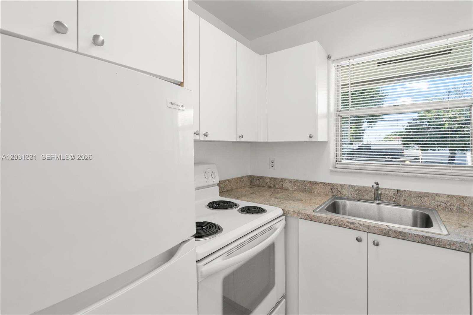 A small kitchen features white cabinets, a white stove, a stainless steel sink, and countertops — 856 SW 10th St # 1, Hallandale Beach FL 33009, HALLANDALE BEACH, FL