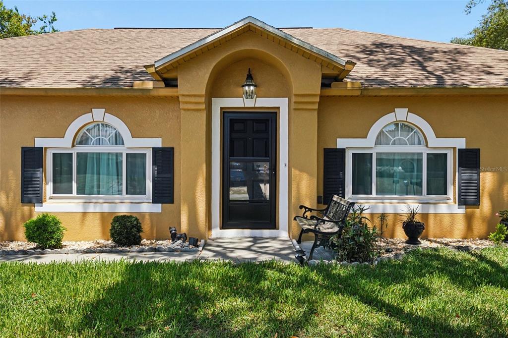 A single-story house with a yellow stucco exterior, black shutters, and a central arched entryway — 10423 BRADFORD STREET, SPRING HILL, FL