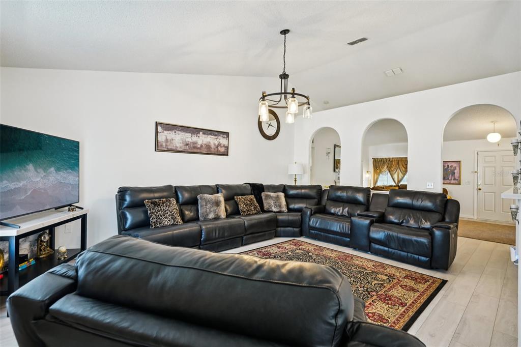 A living room features a large black sectional sofa, a patterned rug, and arched doorways — 10423 BRADFORD STREET, SPRING HILL, FL