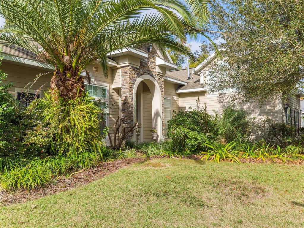 A tan house with a stone-accented arched entryway and a large palm tree in front — 1486 SW 87TH STREET, GAINESVILLE, FL