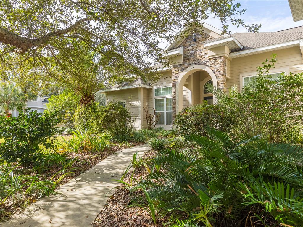A concrete walkway leads to the stone-accented entrance of a tan house with landscaping — 1486 SW 87TH STREET, GAINESVILLE, FL