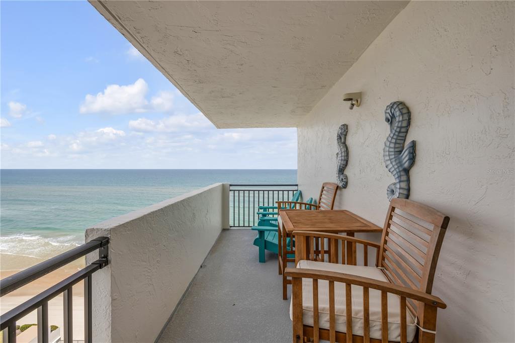 A balcony with wooden chairs and a table overlooks the ocean under a blue sky — 2987 S ATLANTIC AVENUE UNIT 1104, DAYTONA BEACH, FL