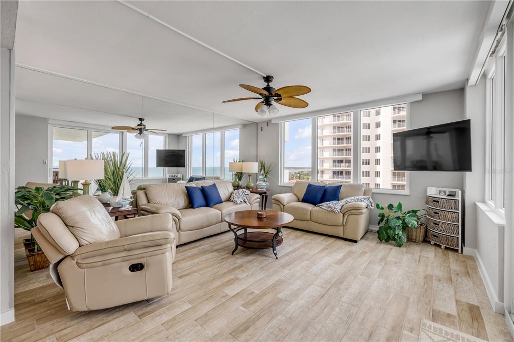 A living room features beige leather furniture, wood-look tile flooring, and floor-to-ceiling windows with ocean views — 2987 S ATLANTIC AVENUE UNIT 1104, DAYTONA BEACH, FL