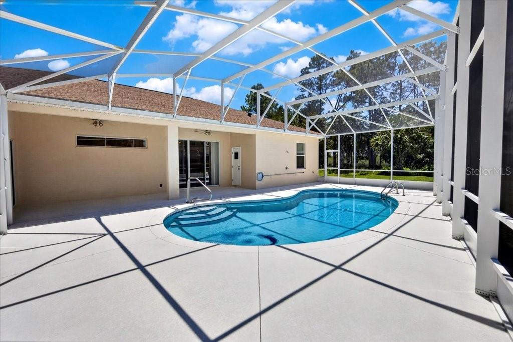 A swimming pool with a screen enclosure sits on a concrete patio behind a house — 25 WESTMINSTER DRIVE, PALM COAST, FL