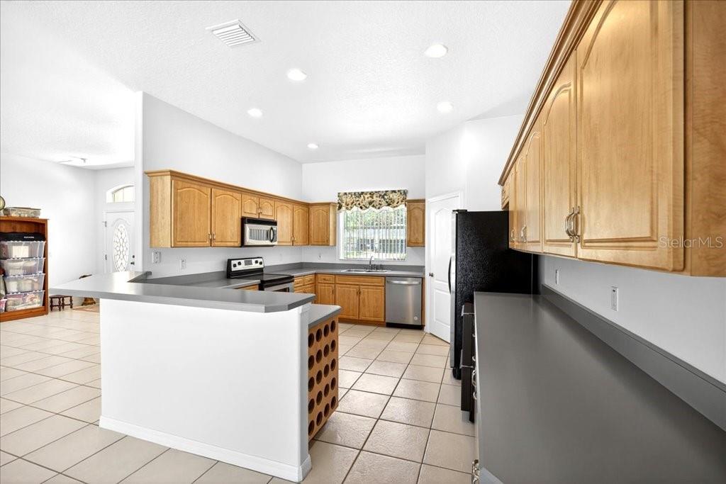 A kitchen with light wood cabinets, gray countertops, tile flooring, and a breakfast bar — 25 WESTMINSTER DRIVE, PALM COAST, FL