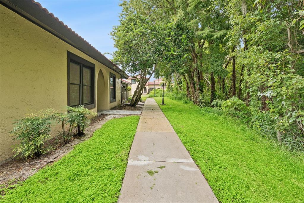 A concrete walkway runs alongside a yellow stucco building next to a wooded area — 530 HUNTER CIRCLE, KISSIMMEE, FL