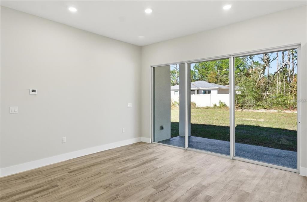 An empty room with light wood-look flooring and large sliding glass doors to a yard — 13205 SW 65TH CIRCLE, OCALA, FL