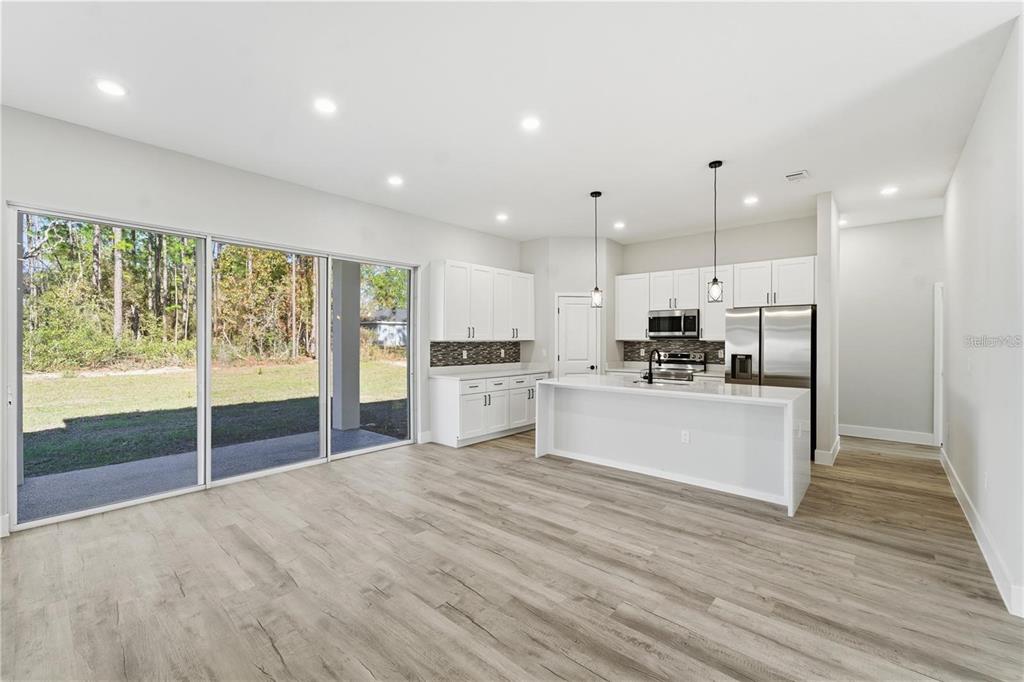 A modern kitchen with white cabinetry, a central island, and sliding glass doors to a yard — 13205 SW 65TH CIRCLE, OCALA, FL