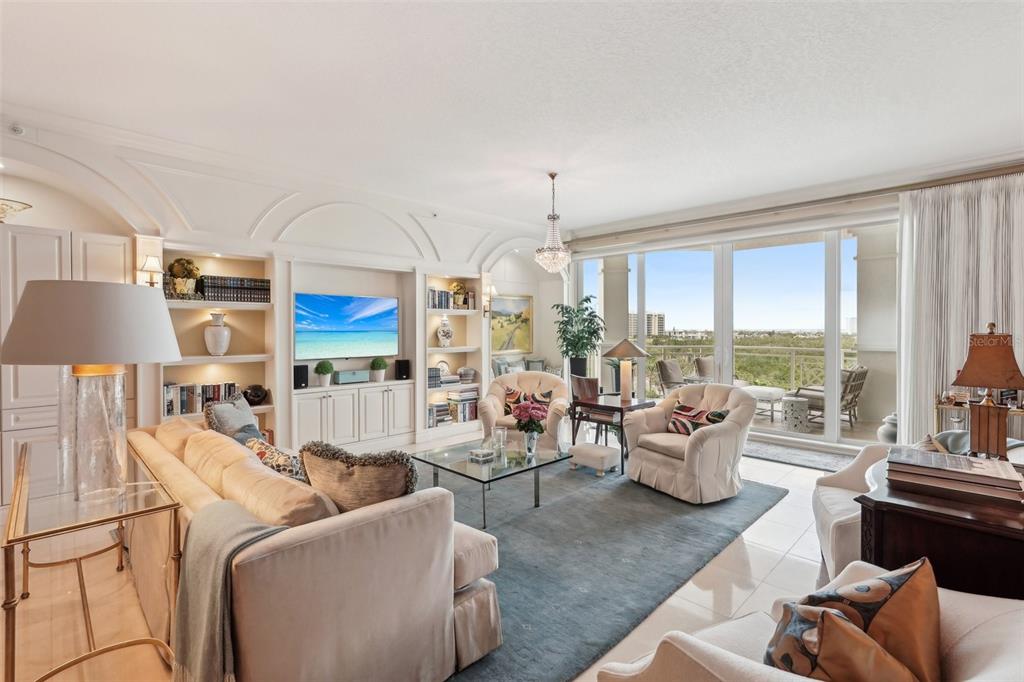 A bright living room features built-in shelving, a large sofa, and floor-to-ceiling windows with balcony access — 2050 BENJAMIN FRANKLIN DRIVE UNIT B704, SARASOTA, FL