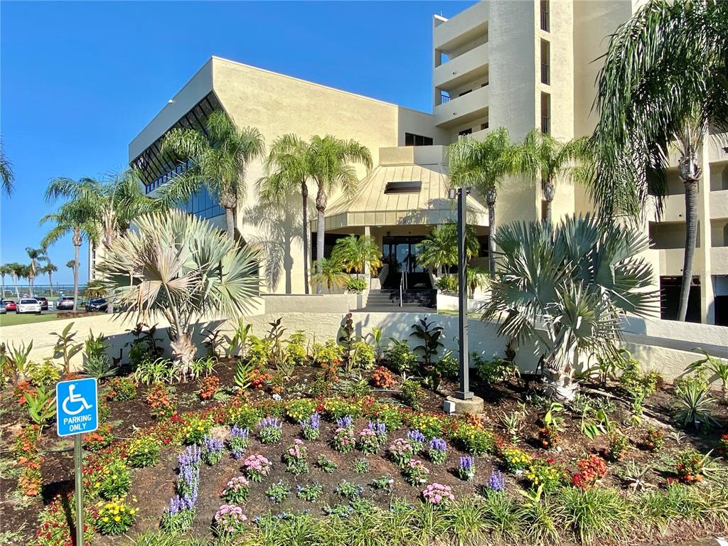 A multi-story beige building features a landscaped garden with palm trees and a handicap sign — 5915 SEA RANCH DRIVE UNIT 509W, HUDSON, FL