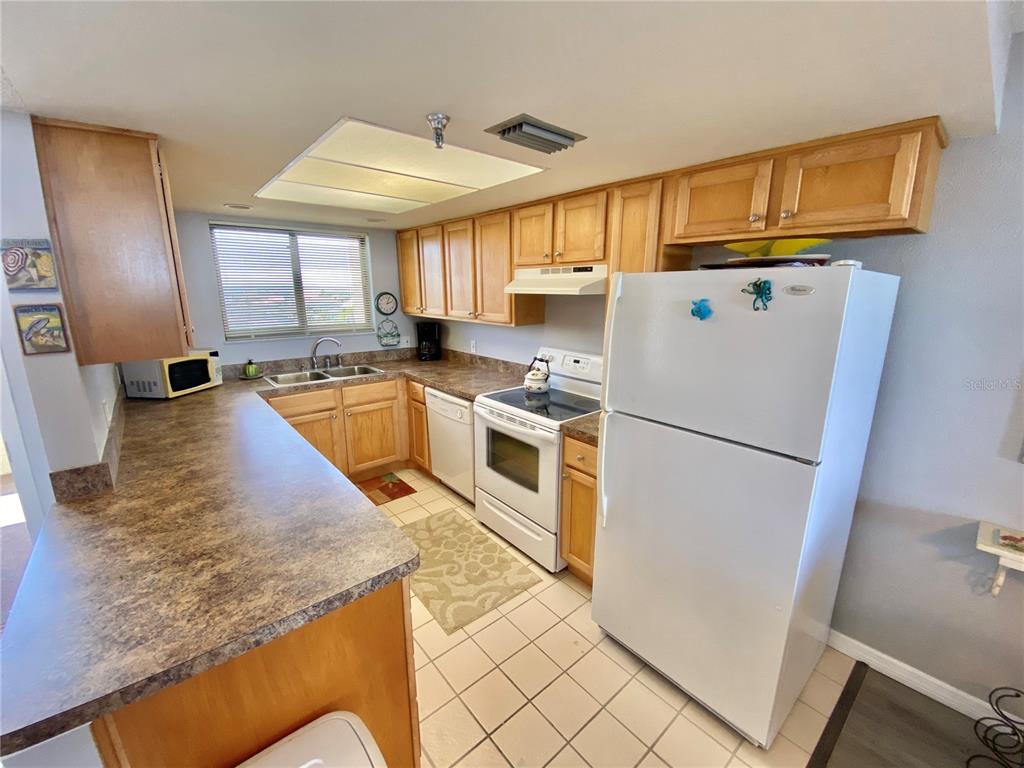 A kitchen with light wood cabinets, laminate countertops, white appliances, and tiled flooring — 5915 SEA RANCH DRIVE UNIT 509W, HUDSON, FL