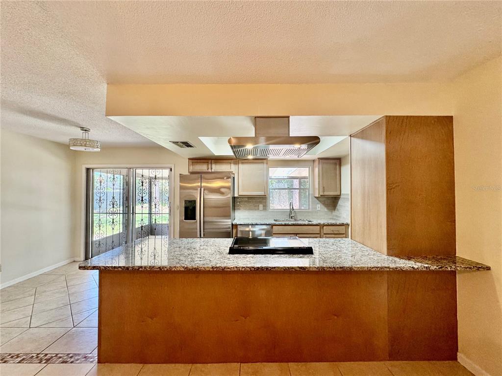 A kitchen features a granite-topped island with a cooktop, stainless steel appliances, and wood cabinetry — 29 FOXHALL LANE, PALM COAST, FL