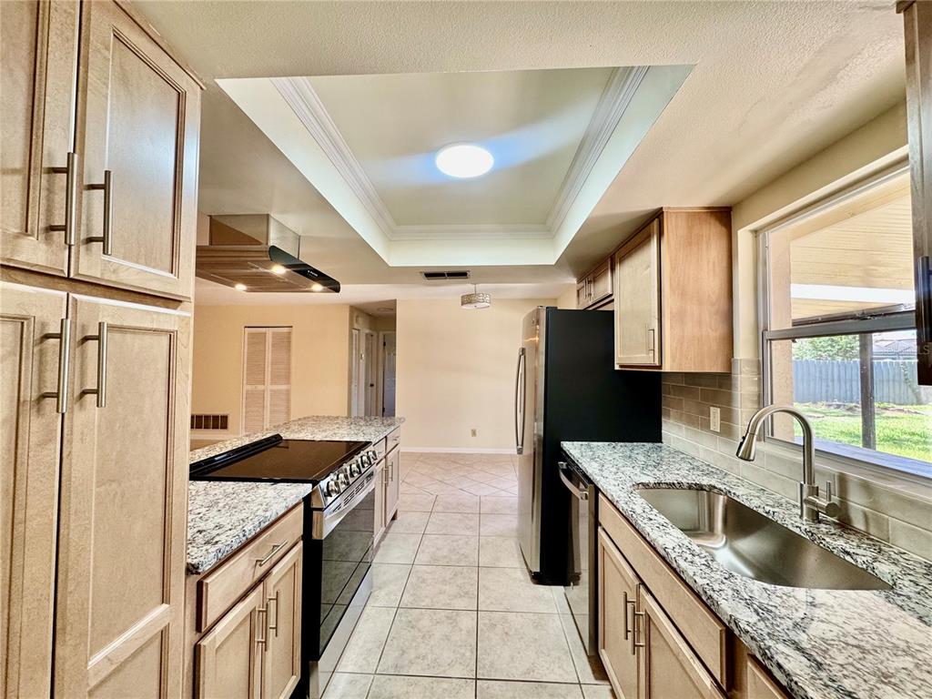 A kitchen features light wood cabinets, granite countertops, stainless steel appliances, and a tray ceiling — 29 FOXHALL LANE, PALM COAST, FL