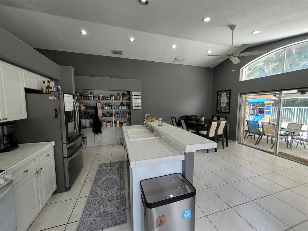 A kitchen with white tile counters and cabinets opens to a dining area and patio — 6416 Barton Creek Circle, Lake Worth FL 33463, LAKE WORTH, FL