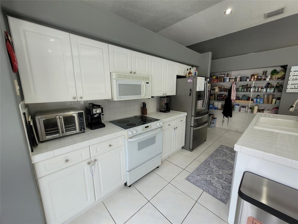 A kitchen features white cabinets, tiled countertops, white appliances, and an open pantry area — 6416 Barton Creek Circle, Lake Worth FL 33463, LAKE WORTH, FL
