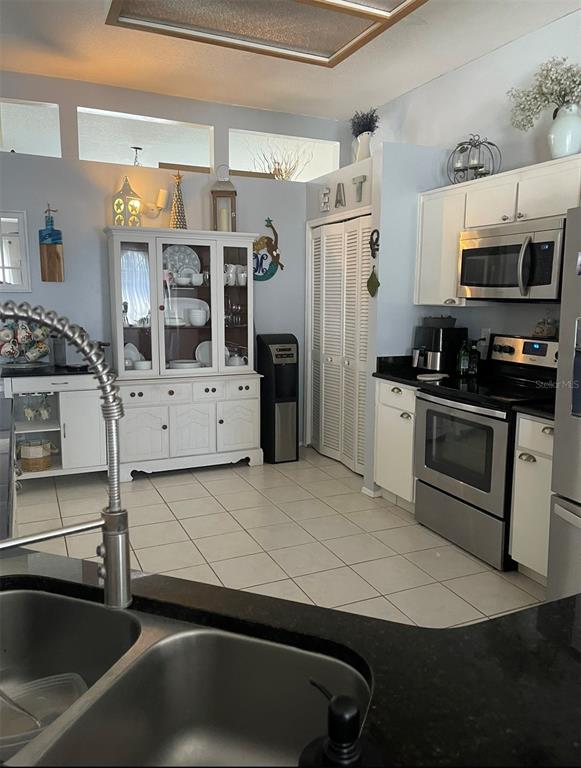 A kitchen features white cabinetry, stainless steel appliances, a hutch, and light-colored tile flooring — 1826 EAGLE RIDGE BOULEVARD, PALM HARBOR, FL