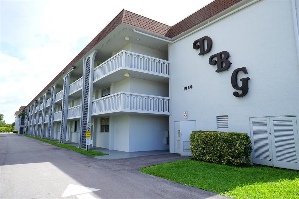 A three-story apartment building exterior with white walls, balconies, and large decorative letters — 1040 SE 4th Avenue # 222, Deerfield Beach FL 33441, DEERFIELD BEACH, FL