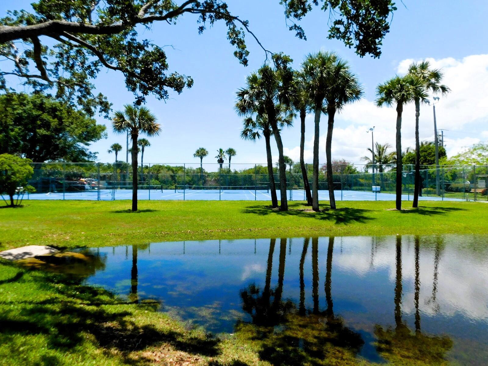 A blue tennis court sits behind a grassy lawn with a reflecting pond in front — 6062 SE Landing Way # 2, Stuart FL 34997, STUART, FL